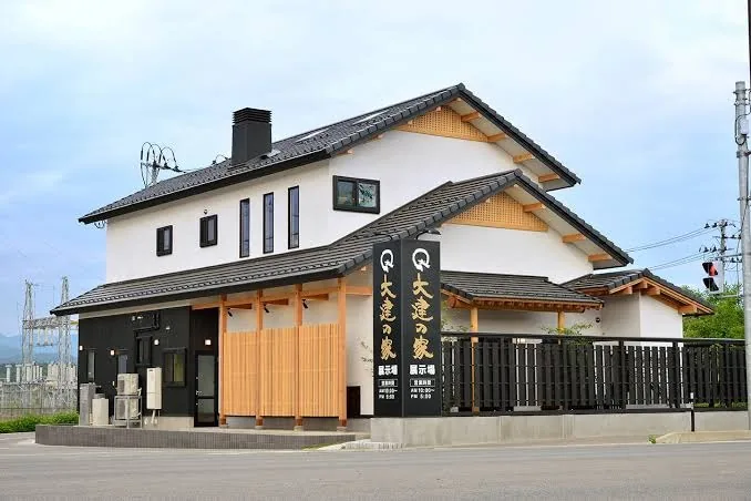 大建の家 展示場の写真。白い壁と黒い外壁、木の格子、瓦屋根の2階建てと「大建の家」の看板